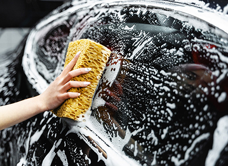 A woman's hand washing a car with a soapy sponge
