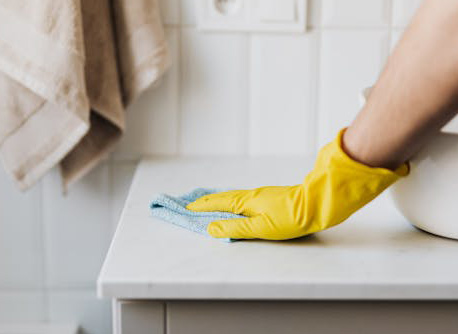 a hand in a yellow rubber glove wipes down a bathroom surface